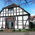 Heimathaus Levern Fachwerkhaus mit markanter Architektur, bunte Tür, gepflegte Vorgartenanlage, blauer Himmel.