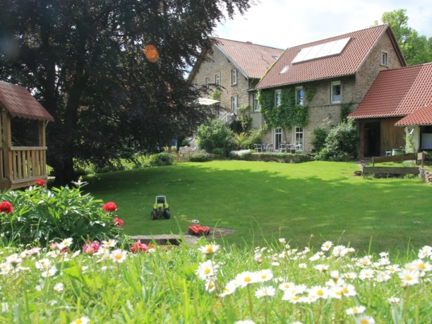 Garten Kaisers Hof Ein üppiger Garten mit blühenden Blumen, Rasen, Spielzeug und einem einladenden, begrünten Steinhaus.