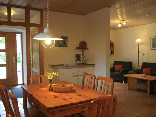 Ein Innenraum mit Holzmöbeln, Essbereich, beleuchtetem Tisch und angrenzender Sitzecke mit Lampen.