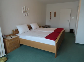 Ein Doppelzimmer mit zwei zusammenstehenden Einzelbetten, weißen Bettdecken und rotem Fußüberwurf.