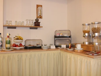 Frühstücksbuffet mit Cerealien, frischem Obst, Backwaren, Aufschnitt, Gläsern und Getränken im Hotel.