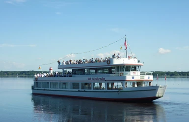 MS Bad Zwischenahn.jpg Die Weisse Flotte mit roten Akzenten, der Name "Bad Zwischenahn" seitlich sichtbar, fährt unter blauem Himmel über einen ruhigen See.