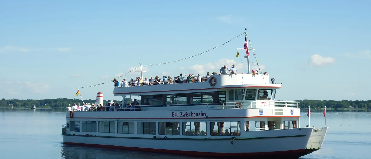 MS Bad Zwischenahn.jpg Die Weisse Flotte mit roten Akzenten, der Name "Bad Zwischenahn" seitlich sichtbar, fährt unter blauem Himmel über einen ruhigen See.