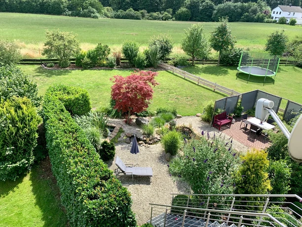 Garten Vogelperspektive eines Gartens mit Rasen, Ziersträuchern, Teich und einem Trampolin im Hintergrund.