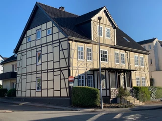 Aussenansicht Fachwerkhaus mit hellem Anstrich und dunklem Dach in einer städtischen Umgebung bei Tageslicht.