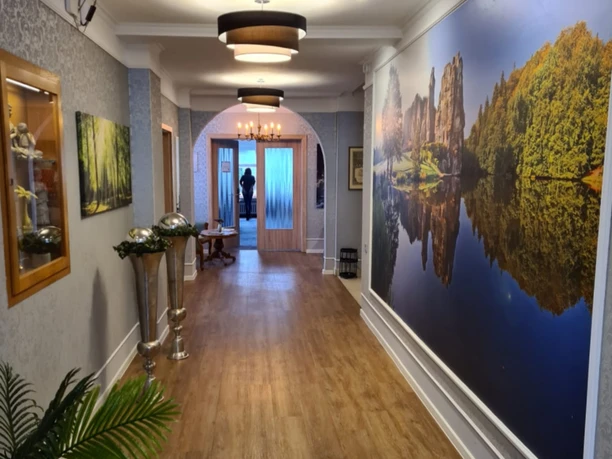 Langer Flur mit Holzboden, dekoriert mit Kunstwerken und Pflanzen, beleuchtet durch elegante Lampen.