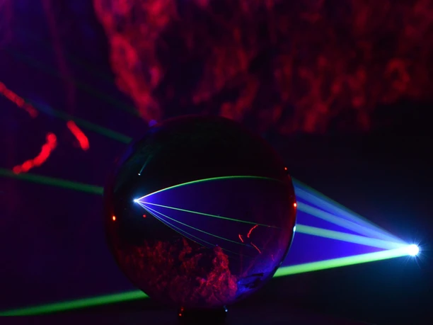 Höhle Glaskugel reflektiert bunte Laserstrahlen in dunkler Höhle mit leuchtenden roten Wänden.