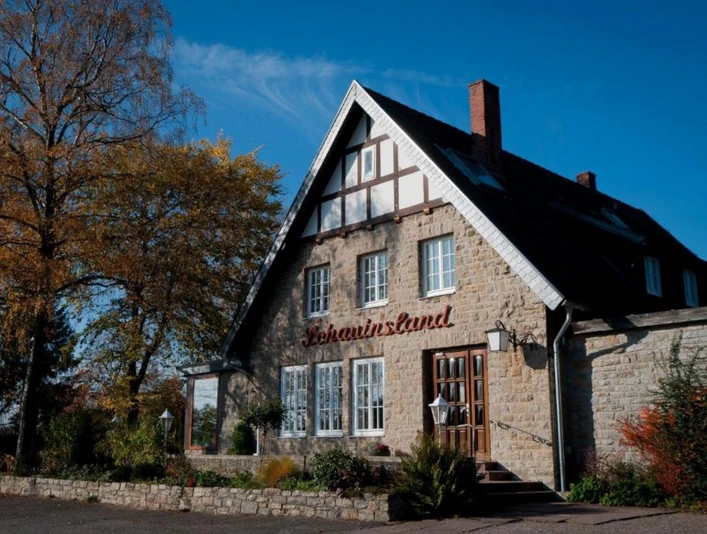 Ein traditionelles Gebäude mit Fachwerk-Elementen, flachem Schieferdach und umgeben von Bäumen.