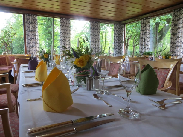 Tafel Ein festlich gedeckter Tisch in einem lichtdurchfluteten Raum mit Blick auf grüne Bäume.