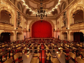 Historische Theaterbühne mit prachtvollem roten Samtvorhang und eleganter Zuschauerbestuhlung.