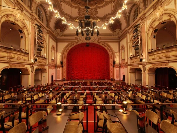 Historische Theaterbühne mit prachtvollem roten Samtvorhang und eleganter Zuschauerbestuhlung.