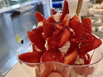 Große Eisportion mit frischen Erdbeerscheiben und Sahne in einer Schale im hellen Eiscafé.