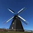 Windmühle Paula mit schwarzen Flügeln und tiefblauem Himmel im Hintergrund, umgeben von Holzzaun.