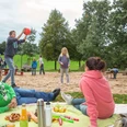 Freizeitpark Langfort in Langenfeld Menschen entspannen auf einer grünen Wiese, während Kinder im Hintergrund Ballspiele auf einem Spielplatz genießen.