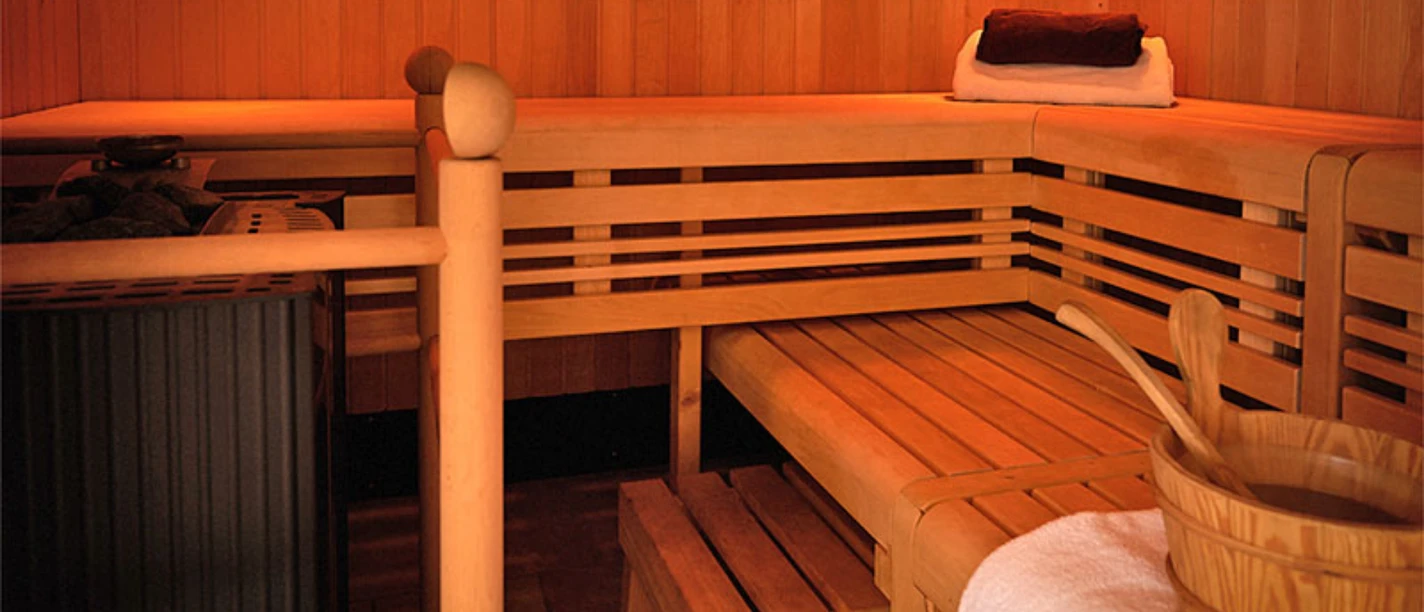 Saunabereich Ein hölzerner Saunaraum mit erhöhten Holzliegen, einem Saunaofen und einem Eimer mit Schöpfkelle.