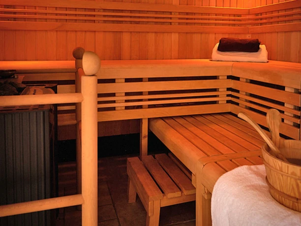 Saunabereich Ein hölzerner Saunaraum mit erhöhten Holzliegen, einem Saunaofen und einem Eimer mit Schöpfkelle.