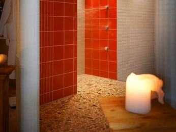 Wellnessbereich Kerzen erleuchten eine moderne Wellnessdusche mit roten Fliesen und pebble Boden, strahlend einladend.