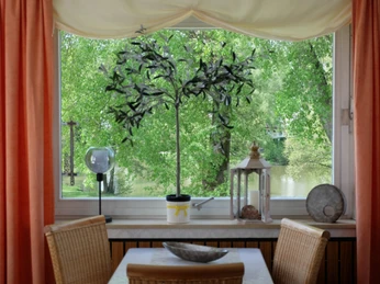 Ein Frühstückszimmer mit einem Fensterblick auf einen grünen See, dekoriert mit Pflanzen und Laternen.