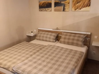 Gemütliches Schlafzimmer mit Doppelbett, karierten Bettdecken und Strandbildern an der Wand.