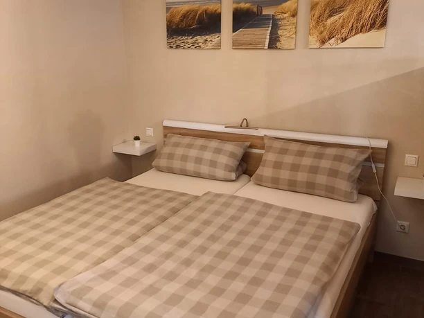 Ferienwohnung Zum Alten Graf_Schlafzimmer Gemütliches Schlafzimmer mit Doppelbett, karierten Bettdecken und Strandbildern an der Wand.