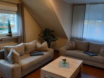 Gemütliches Wohnzimmer mit zwei großen beigefarbenen Sofas, Holztisch und Fensteraussicht auf Bäume.