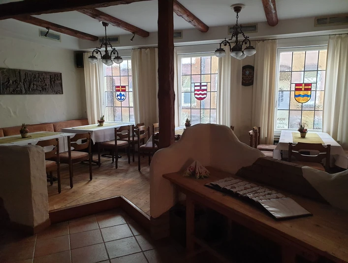 IMG-20220316-WA0000 Pilsquelle.jpg Ein traditioneller Gastraum mit Holzmöbeln, dekorativen Fenstern und gedämpfter Beleuchtung.