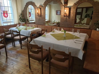 IMG-20220316-WA0002 Pilsquelle.jpg Ein rustikaler Gastraum mit Holztischen, grünen Tischdecken, Gläsern und traditionellen Dekorelementen.