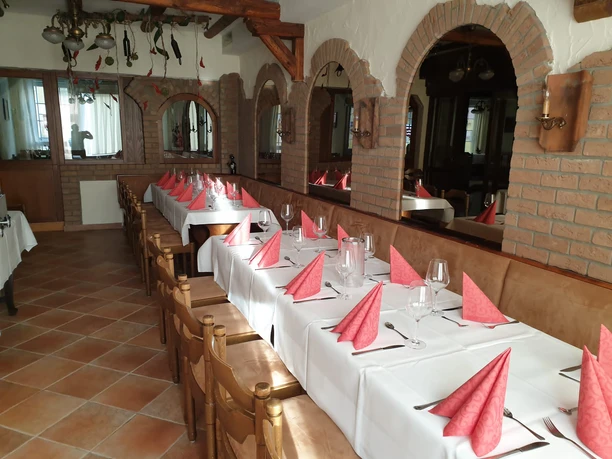 IMG-20220316-WA0001 Pilsquelle.jpg Ein langer Esstisch in einem festlich gedeckten Raum mit roten Servietten und rustikalem Interieur.