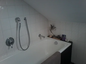 Badewanne mit Duschkopf in einem Badezimmer mit weiß gefliester Schräge und minimalistischem Dekor.