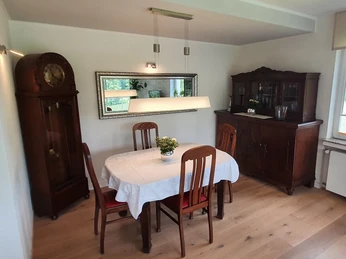 Ein Essbereich mit Holztisch und Stühlen, umgeben von antiken Möbeln, darunter ein hoher Uhrenschrank.