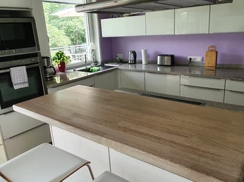 Küche Moderne Küche mit großer Holzarbeitsfläche, weißen Schränken und lila Wand, Blick ins Grüne.