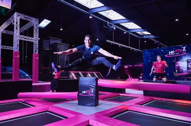 Hi-Fly Trampolin Park in Hilden Ein Trampolinpark mit leuchtenden pinken Elementen und fröhlich springenden Personen, die Spaß haben.