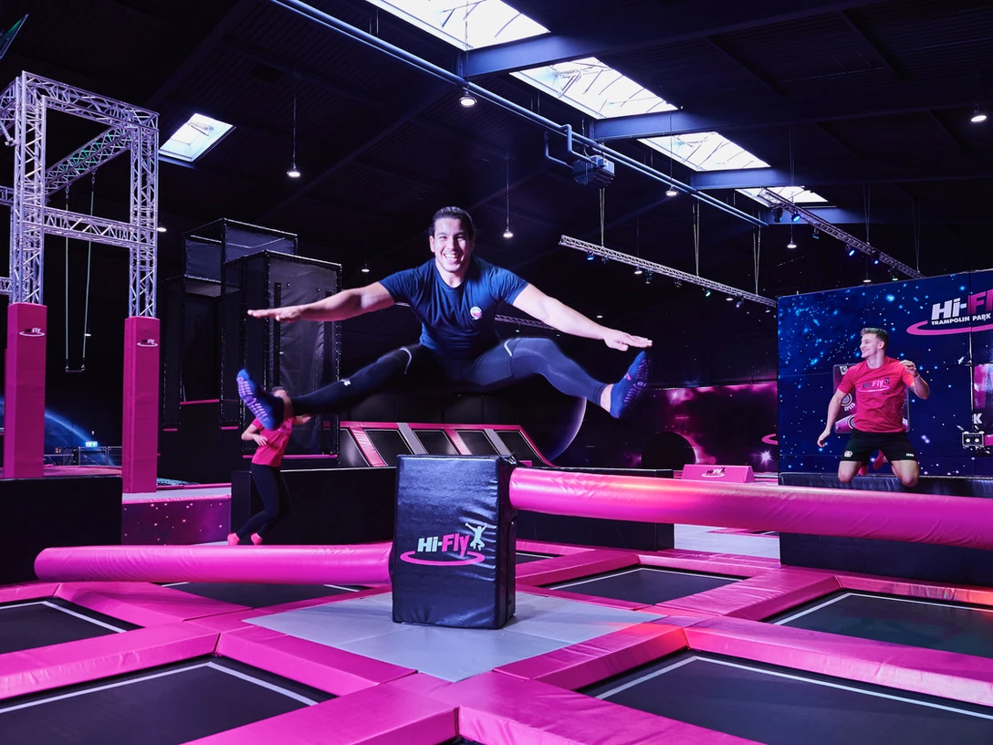 Hi-Fly Trampolin Park in Hilden Ein Trampolinpark mit leuchtenden pinken Elementen und fröhlich springenden Personen, die Spaß haben.