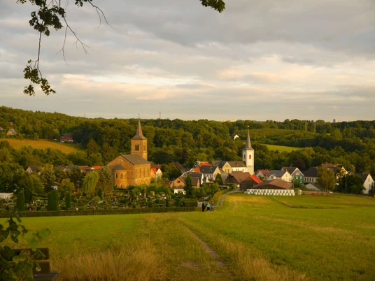 Wülfrath-Düssel Panorama von Wülfrath-Düssel mit Kirche, bunten Häusern und grünem, hügeligem Umland bei Sonnenschein.