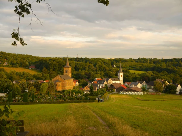 Wülfrath-Düssel Panorama von Wülfrath-Düssel mit Kirche, bunten Häusern und grünem, hügeligem Umland bei Sonnenschein.