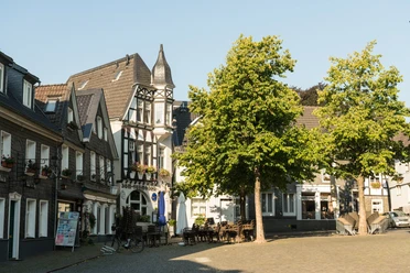 Kirchplatz der Oberstadt in Mettmann Historische Fachwerkgebäude und Bäume säumen den Kirchplatz in Mettmann bei klarem Himmel.