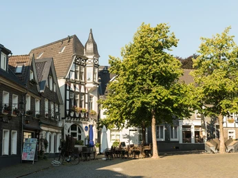 Kirchplatz der Oberstadt in Mettmann Historische Fachwerkgebäude und Bäume säumen den Kirchplatz in Mettmann bei klarem Himmel.