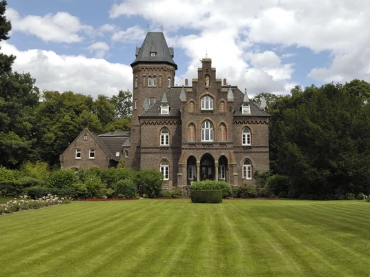 Marienburg mit Marienburgpark in Monheim am Rhein Eine imposante Backsteinburg mit kleinem Turm, umgeben von gepflegtem Rasen und Bäumen.