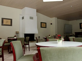 Ein stilvoll eingerichtetes Zimmer mit einem modernen, weißen Kamin, grüne Stühle und runde Tische.