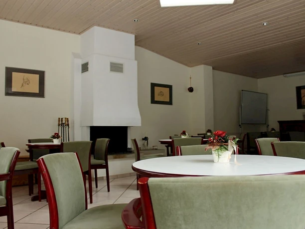 Kaminzimmer Ein stilvoll eingerichtetes Zimmer mit einem modernen, weißen Kamin, grüne Stühle und runde Tische.