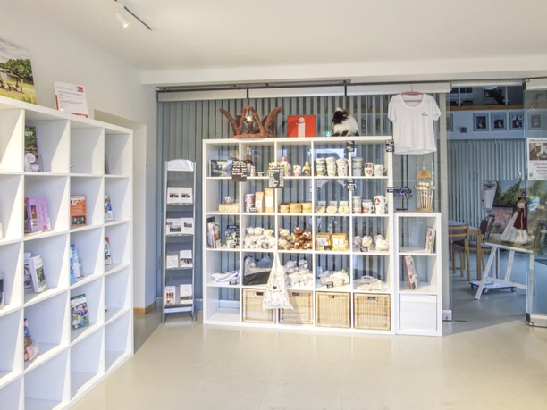 Innenansicht In einem hellen Raum mit modernen, weißen Regalen werden lokale Produkte und Souvenirs stilvoll präsentiert. Ein großes Schiebetor aus Glas im Hintergrund trägt zur offenen und einladenden Atmosphäre bei.