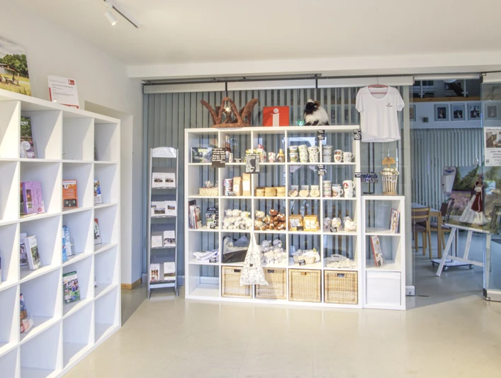 Innenansicht In einem hellen Raum mit modernen, weißen Regalen werden lokale Produkte und Souvenirs stilvoll präsentiert. Ein großes Schiebetor aus Glas im Hintergrund trägt zur offenen und einladenden Atmosphäre bei.