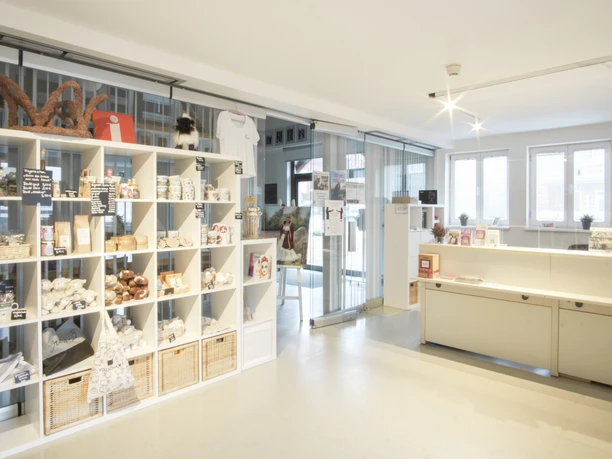 Innenansicht Ein moderner Empfangsbereich mit weißen Regalen voller Souvenirs, einem Tresen und großen Fenstern.