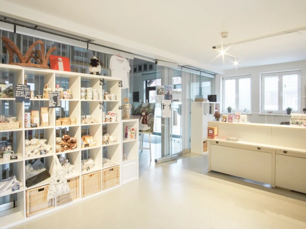 Innenansicht Ein moderner Empfangsbereich mit weißen Regalen voller Souvenirs, einem Tresen und großen Fenstern.