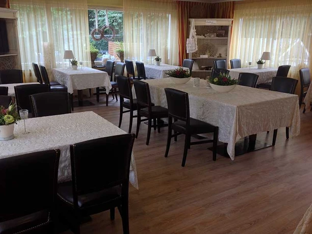 Speisesaal.jpg Ein lichtdurchfluteter Speisesaal mit gedeckten Tischen und schwarzen Stühlen, umgeben von großen Fenstern.