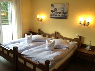 Ein Doppelzimmer mit Holzbett, weißer Bettwäsche, gelben Wänden und romantischem Engelbild an der Wand.