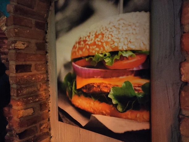 Das Bild eines Burgers mit Zwiebeln, Tomate, Bulette und Käse an einer Wand