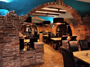 Ein Raum in einem Restaurant mit vielen Stühlen, die mit schwarzem Leder bezogen sind, mit Tischen und an den Wänden sieht man Backsteinmauern