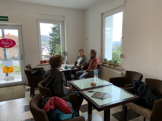 Cafe Teke Innenbereich Drei Personen sitzen an einem Tisch in einem hellen Café mit großen Fenstern und modernem Mobiliar.