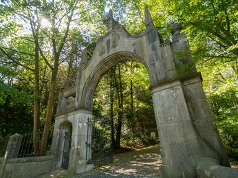 Torbogen von Schloss Landsberg bei Ratingen Torbogen aus Stein, von Grün umgeben, führt auf einen Weg; Lichtakzente durch strahlende Sonne.